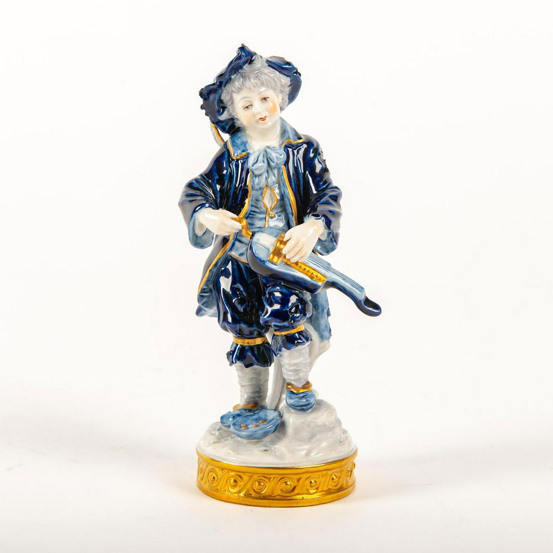 Aelteste Volkstedt Porcelain Figurine, Musical Peasant: Hand painted, glazed blue with accents of gold gilt depicting a peasant boy playing his lute for money. On round gilded base with scroll designs in high-relief. Blue Volkstedt mark to bottom base. Imp