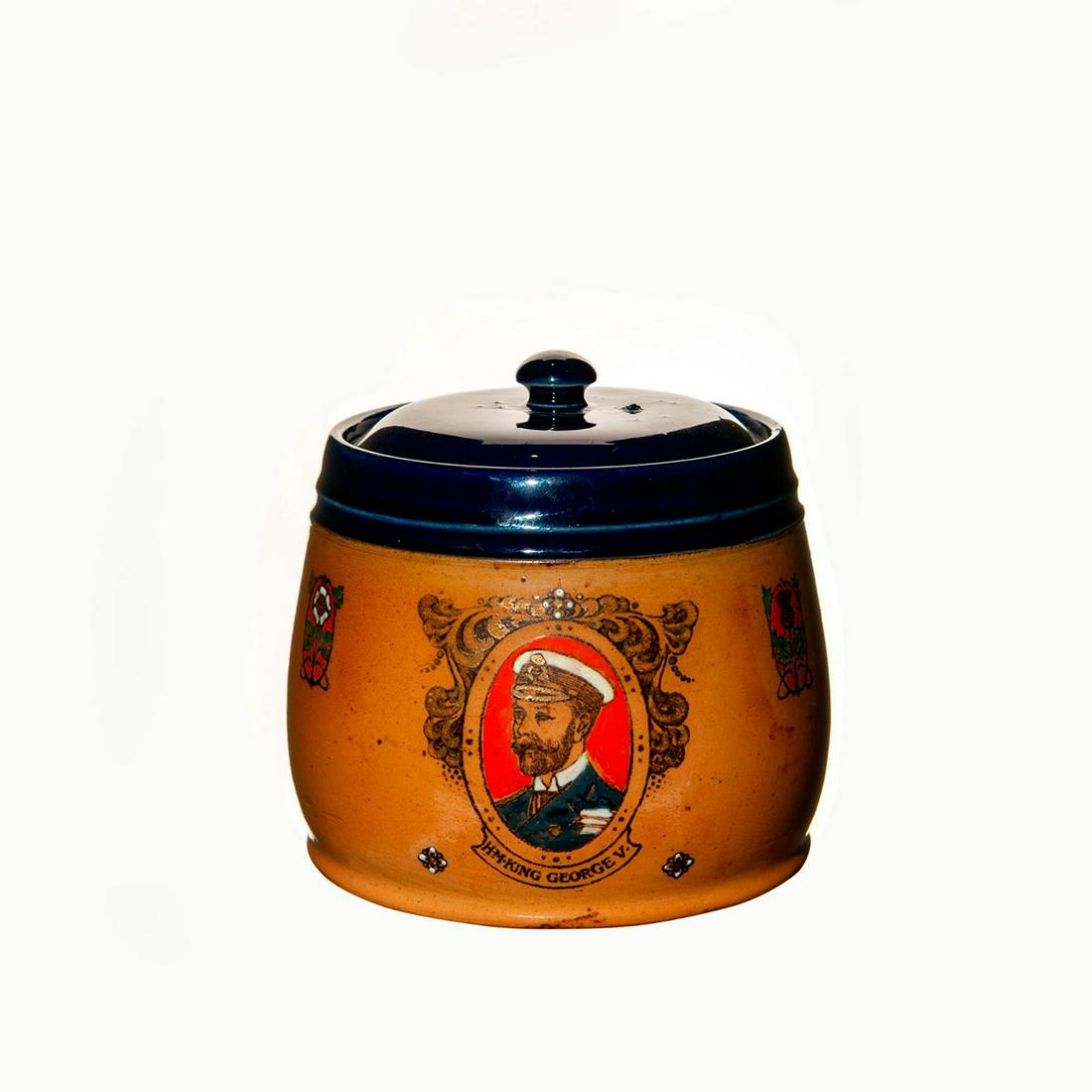 Royal Doulton King George V Lidded Tobacco Jar: Regal Royal Doulton jar with portraits of King George V and Queen Mary. The stoneware body is complimented with a Royal Blue band at the rim and lid. Both portraits use bright orange as a background t