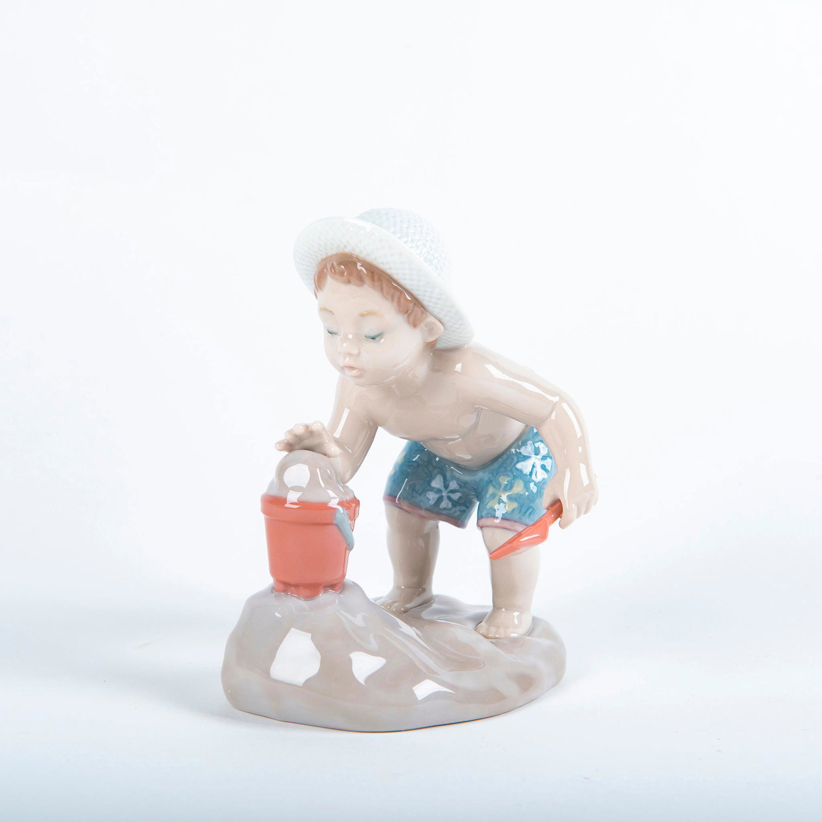 Playing In The Sand 01008440 - Lladro Porcelain Figure: Glossy porcelain figurine; Child enjoys some fun in the sand. Lladro backstamp. Includes original box. Artist: Jose Santaeulalia Issued: 2009 Dimensions: 4.75"H Manufacturer: Lladro Country of Origin: