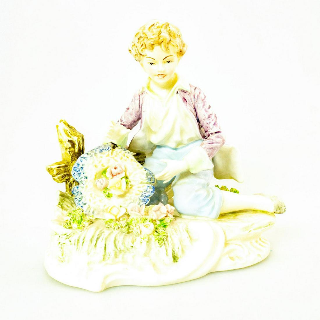 Fine Porcelain Figurine, Boy Sitting With Flowers: Hand painted porcelain of a boy in purple, white and blue; Sitting with flowers near fence. Unidentified black crossed arrow backstamp marked M4050. Tip of left hand pinky finger missing. Issued: 20th