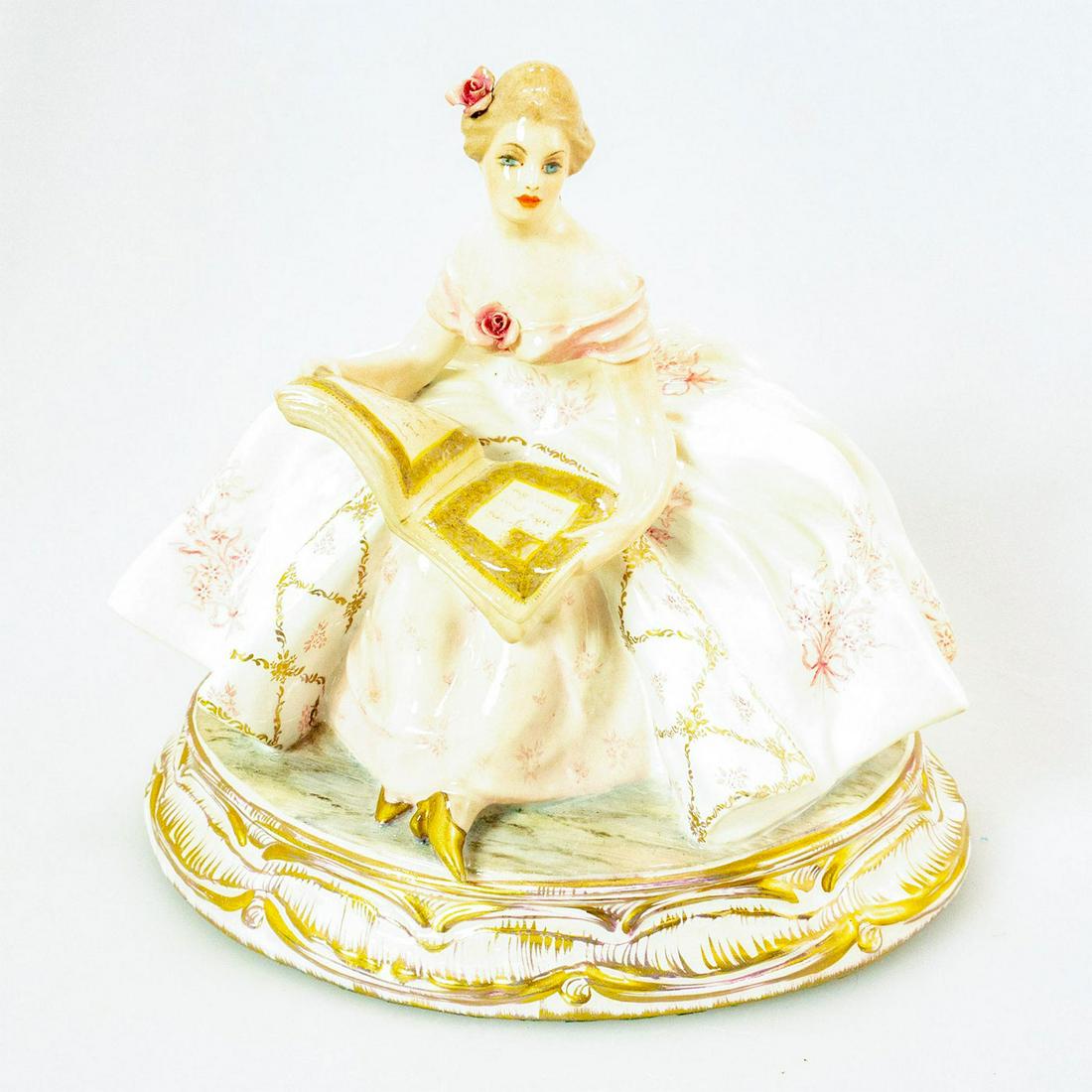 Vintage Guido Cacciapuoti Figurine, Woman Reading: Italian porcelain figure of a woman with a book in hands. Pink and white colorway; gilt accents. Soft pastel coloration; intricate floral accents. Cacciapuoti backstamp. Chip to petal. Artist: Guido C
