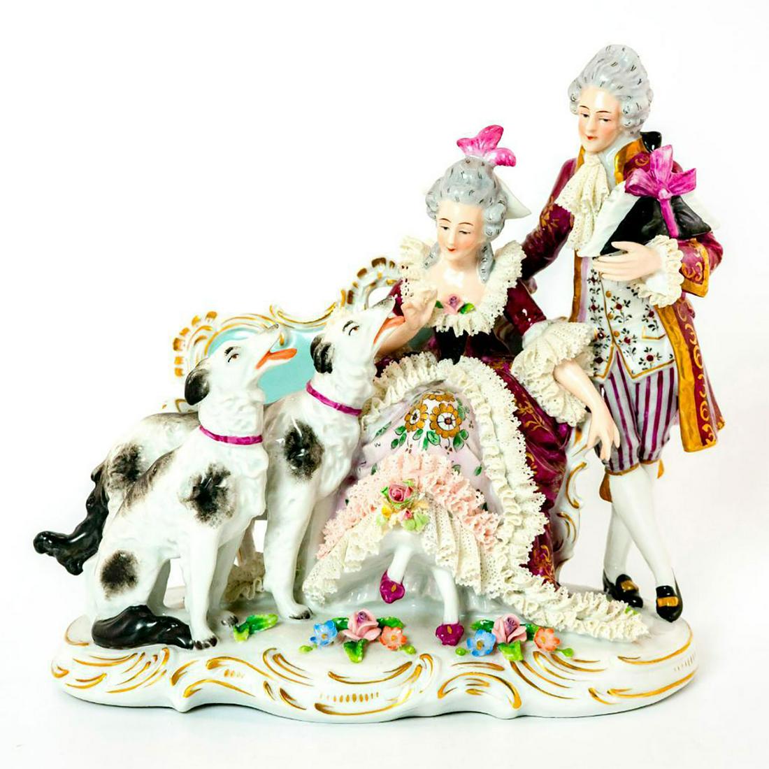 Sitzendorf German Figurine Grouping, Couple With Dogs: Hand painted figural group; couple with borzoi dogs. Impressive modeling; porcelain lace trim. Finely detailed features; vibrant colors; applied flowers. Sitzendorf backstamp. Chipped flowers. Issued: