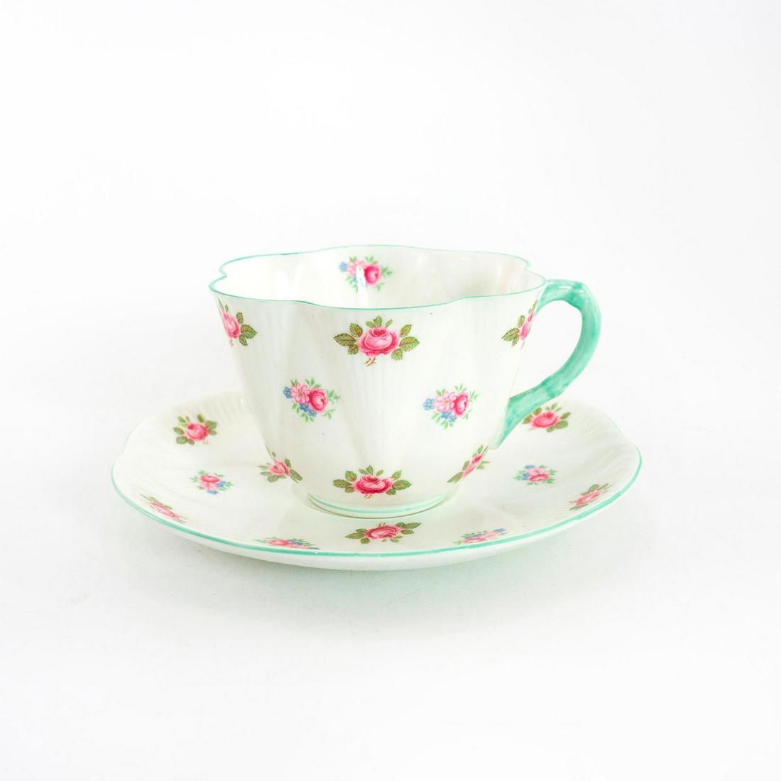 Shelley Fine Bone China Dainty Cup And Saucer, Rosebud: Rosebud pattern; no. 13426. Glazed bone china cup and saucer, with pink and blue flora; green trim. Shelley backstamp. Faint hairline to rim. Issued: 20th c. Dimensions: 2.25"H x 5.5" dia. Manufacture