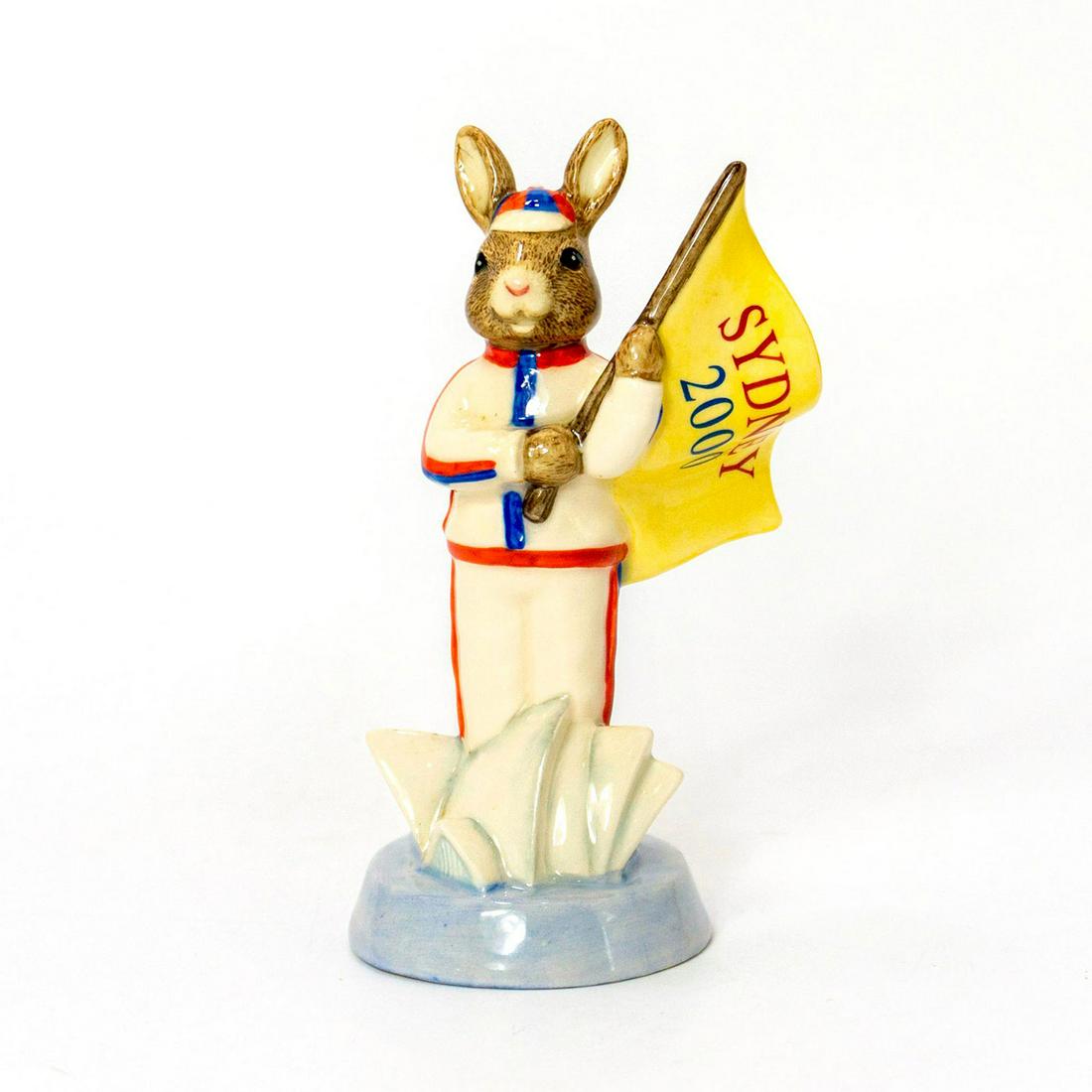 Royal Doulton Bunnykins, England Athletes 2000 Sydney: Limited Edition white blue and red rabbit holding a yellow flag. Edition number 1239 of 2500 with certificate in original box. Royal Doulton backstamp. Artist: Kimberley Curtis Issued: 2000 Dimensions