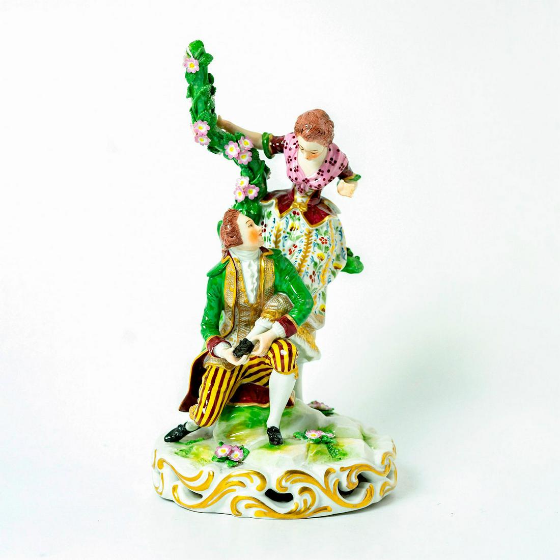 Meissen Style Porcelain Figurine: Man is helping a woman with her shoe. Green, dark red, pink, yellow and gold colorations. Delicate pink flowers on vine and base. Letter "R" stamped on bottom. Damage on flower petals. Woman's thumb i