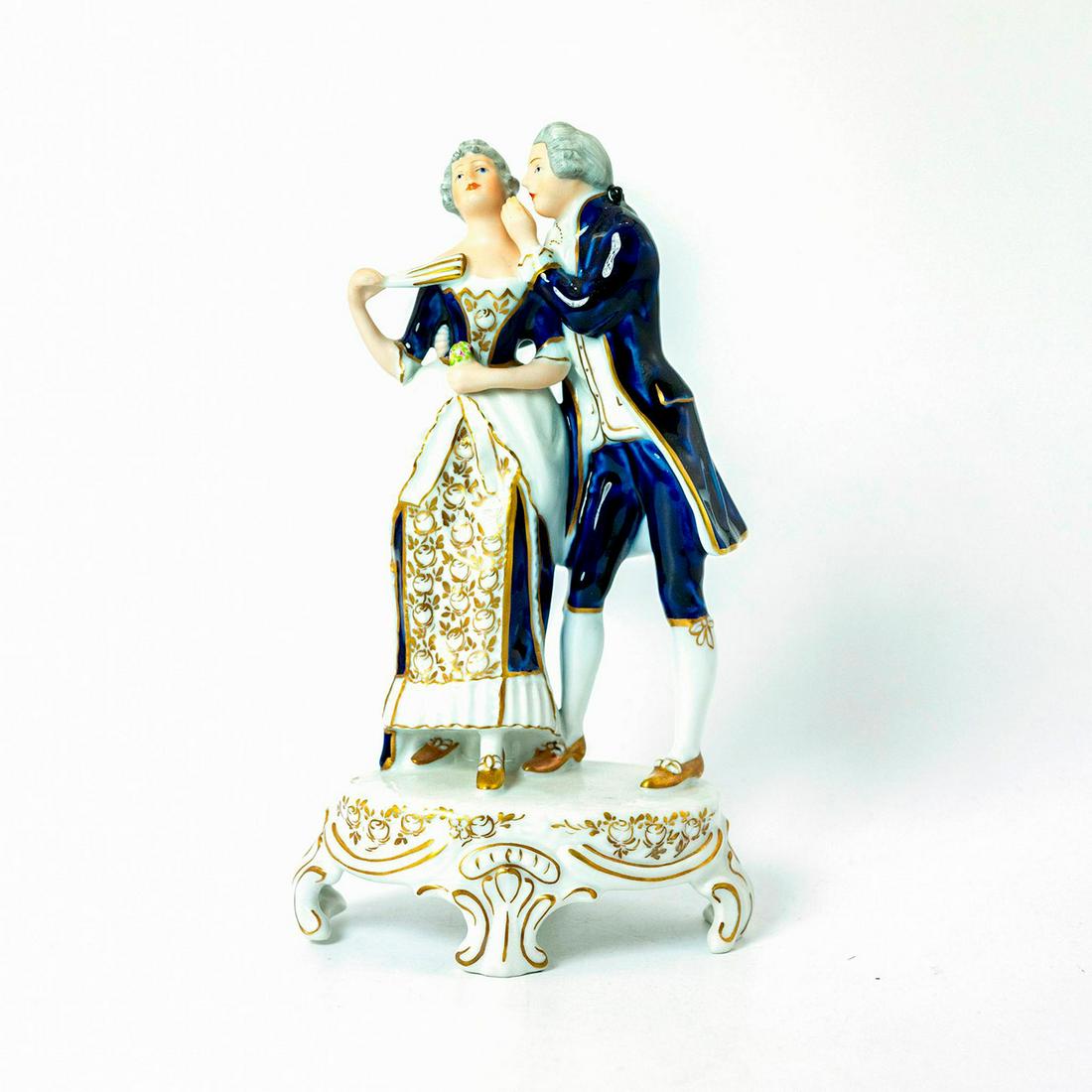 Royal Dux Porcelain Figurine: Man and woman both dressed in royal blue, white and gold clothing in gloss finish. Arms and faces are in matte finish. He is whispering in her ear. Royal Dux backstamp. Issued: 1970-1992 Dimensions: 9