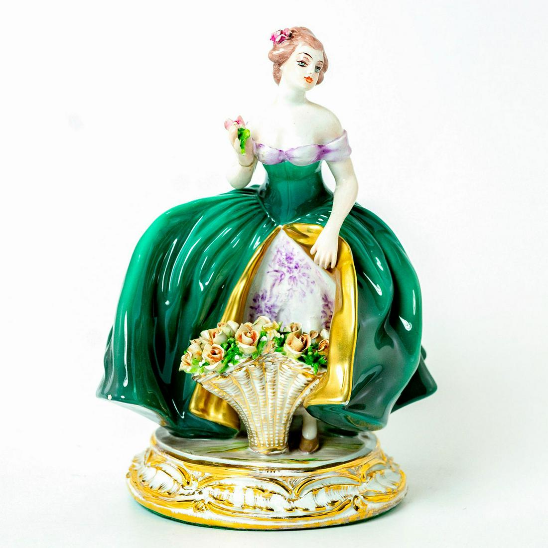 Guido Cacciapuoti Figurine, Woman With Flowers: Glazed porcelain; green, white and purple coloration; applied flowers; gilt accents. Raised on circular gilt base. Signed Cacciapuoti. Chipped petals. Artist: Guido Cacciapuoti Issued: 20th c. Dimensi