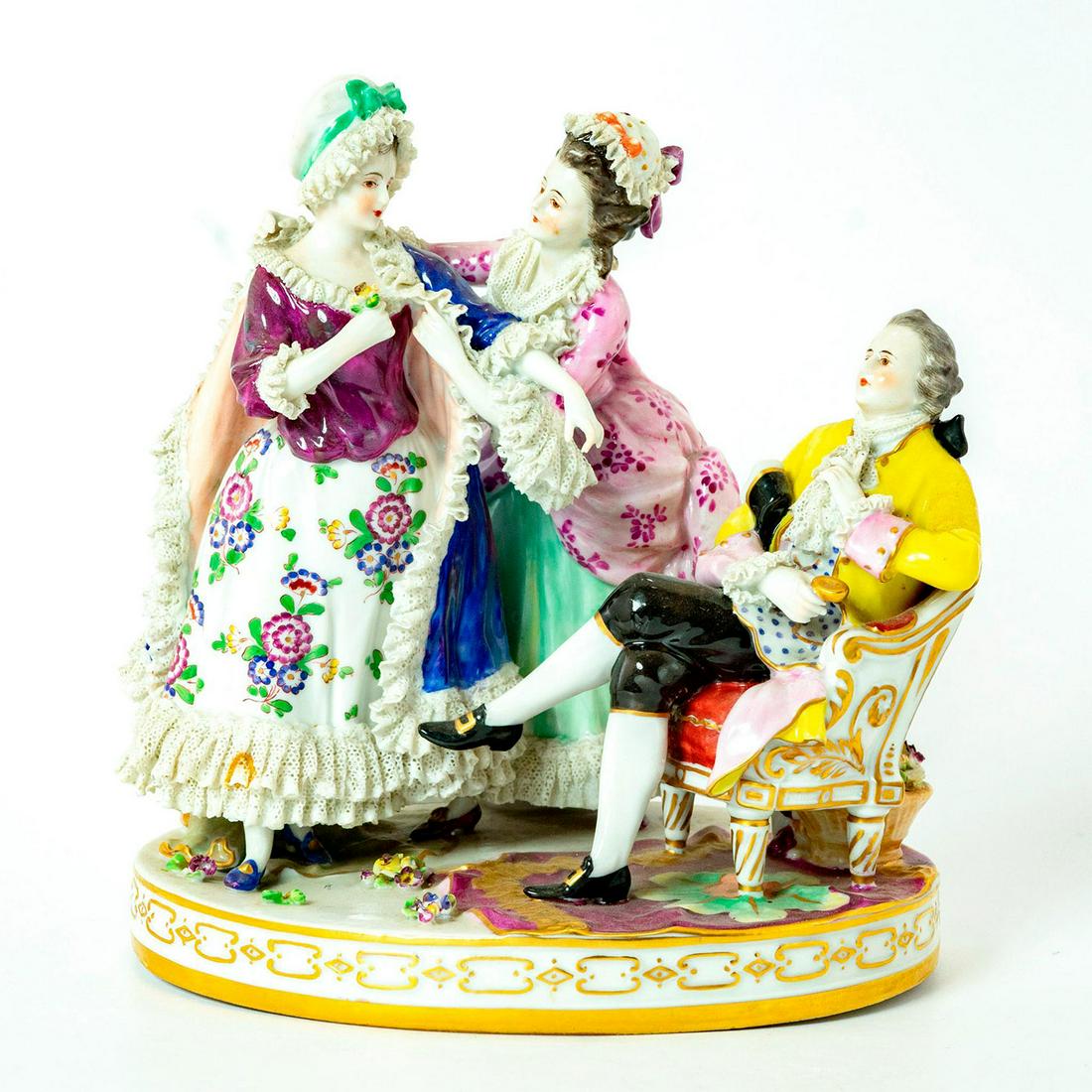Volkstedt Lace Porcelain Figurine: Lovely lady in pink and green floral dress helping another woman into her blue lace coat. A man in a yellow and brown suit is seated on a chair, flower basket beneath it. 1762 Volkstedt style backstam