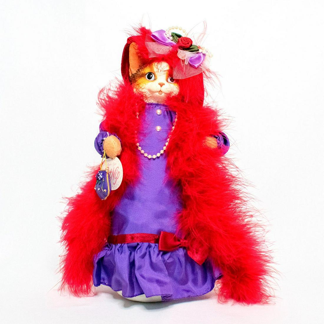 Heather Hykes Cat Nip Ceramic Doll, Molly: Plush doll with weighted bottom and ceramic face. Molly wears a purple dress with a red feather boa. The doll carries a small purse in the right paw and wears a red hat with tulle, ribbon, and pearl b