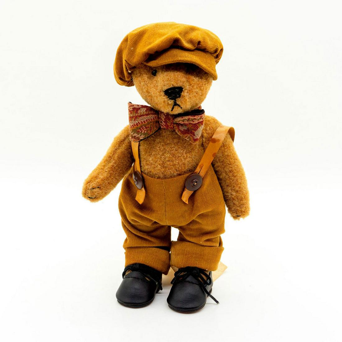 The Paisley Bear Teddy Bear, Sterling: Fully jointed, plush, glass eyes, sewn nose and mouth. Wearing overalls, a paisley bowtie, and a cap. Original tag attached. Issued: 1989 Dimensions: 9"H Manufacturer: The Paisley Bear Country of Orig