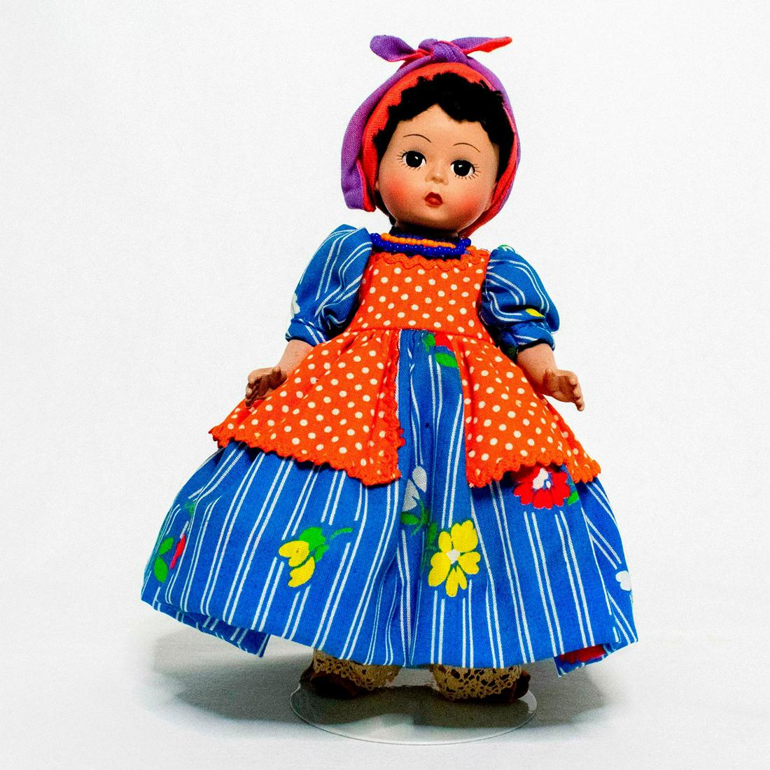 Madame Alexander Doll, Jamaica: Doll with dark eyes and hair. She wears a blue and white striped dress with orange polka dot jumper. She has a full voluminous petticoat beneath her skirt, with lace-trimmed pantaloons, and sandals. H