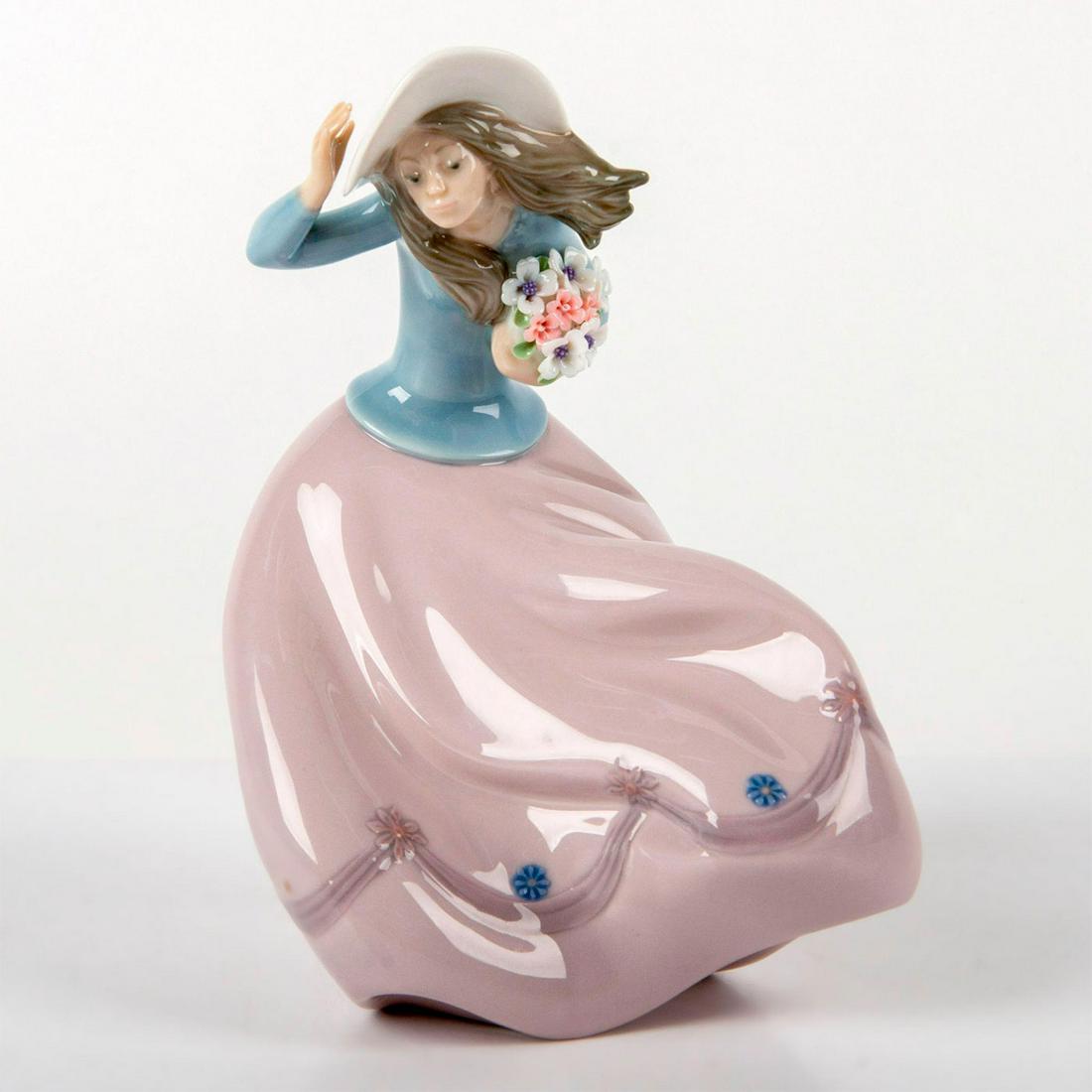 Blustery Day 1005588 - Lladro Porcelain Figurine: A young lady in a wide-brimmed hat holds her bouquet in the wind. Comes with original box. Lladro backstamp. Missing paint on one blue flower on the skirt. Artist: Joan Coderch Issued: 1989 - 1993 Dim