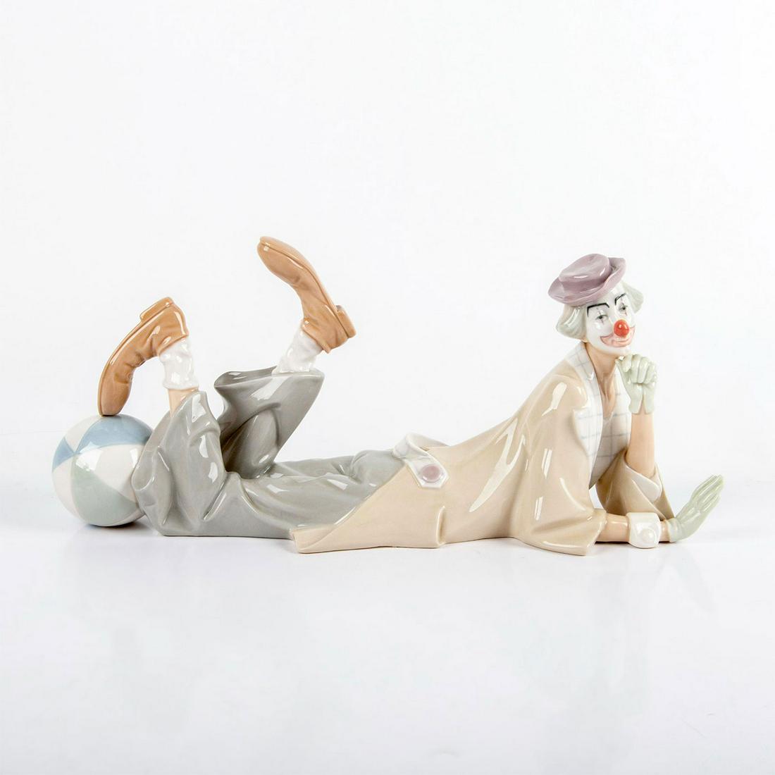 Clown 1004618 - Lladro Porcelain Figurine: Glazed finish. Clown in beige and gray suit laying down with his foot on a blue and white ball. Lladro backstamp. No original box. #clown #ball #lladro Artist: Salvador Furio Issued: 1970-2019 Dimensi