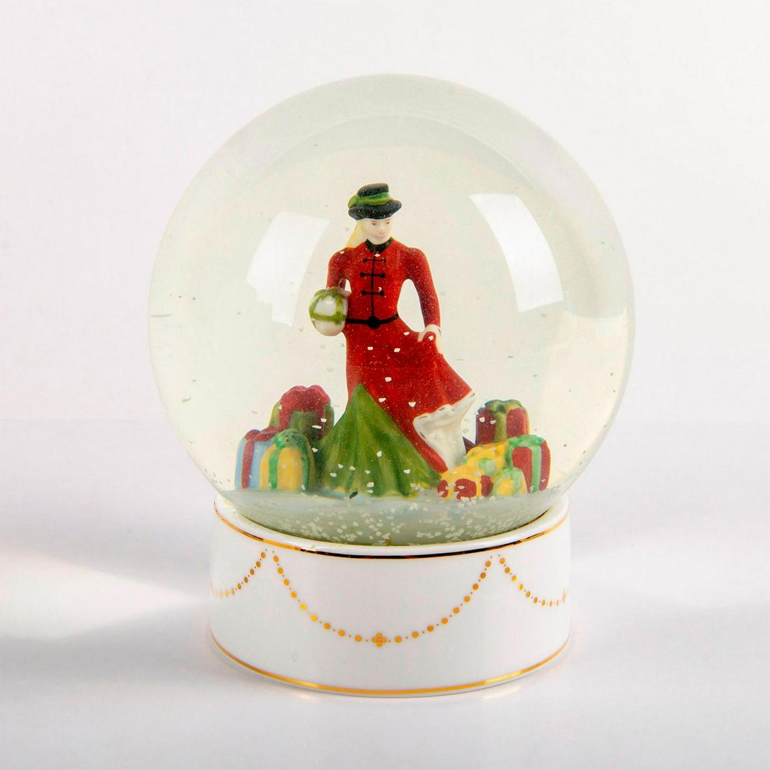 Christmas Gifts Snow Globe HN5524 - Royal Doulton: Snow globe with a woman in a green dress and red overcoat, next to groups of presents. Artist: Doulton Studios Issued: 2011 Dimensions: 5.5"H Edition Number: 445 Edition Size: 2000 Manufacturer: Royal