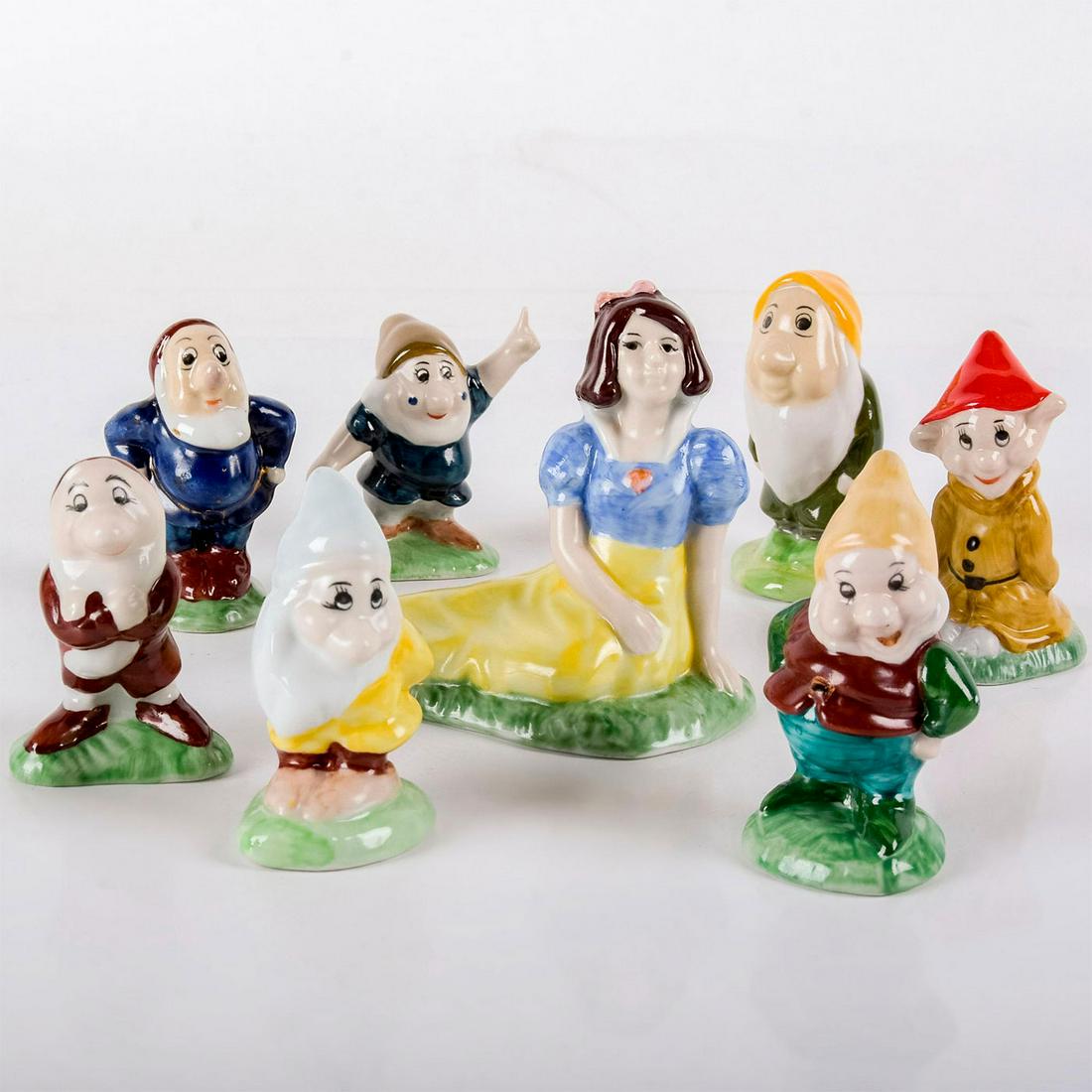 8pc Figurine Set, Snow White And The Seven Dwarfs: Glossy porcelain; in style of Wade bone china. All stand on green bases. No markings. Age related wear. Snow White: 4"H x 4.5"L. Seven Dwarfs: range from 3" - 3.5"H. #snowwhite #porcelain #disney #fig
