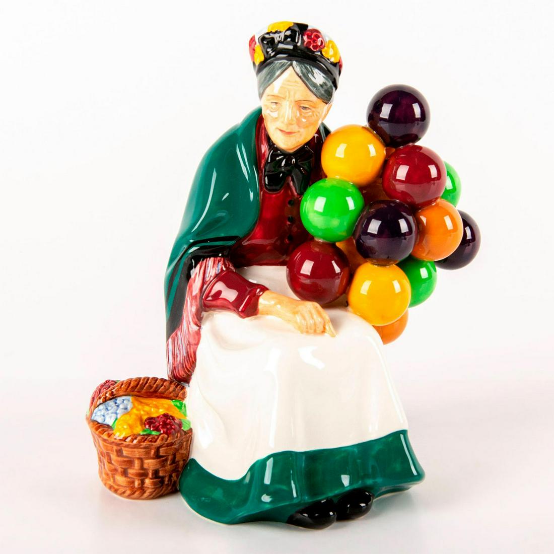 Old Balloon Seller HN1315 - Royal Doulton Figurine: She wears a green shawl over her burgundy blouse and matching white and green skirt. Holding a bunch of colorful balloons for sale. Introduced in 1929, Old Balloon Seller HN1315 is probably the best k