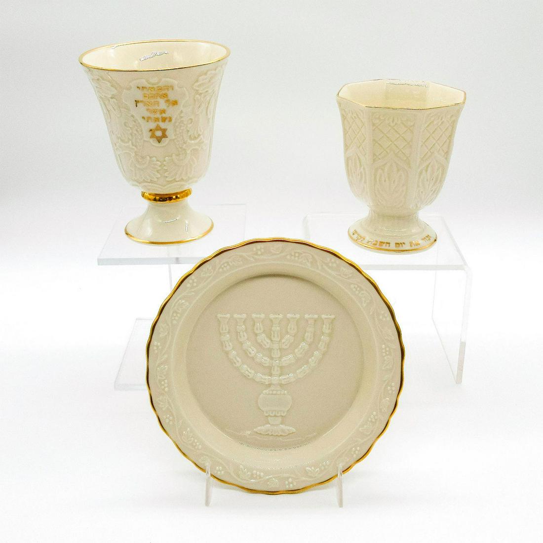 Set of 3 Lenox Hanukkah Themed Dishware: One wine bottle coaster and two Kiddush cups. Porcelain hand decorated with 24K gold. Lenox backstamps. Good condition. Small cup: 4.5"H. Large cup: 5.25"H. Coaster: 6.25"D. Weight: 1 lb 11.2 oz #leno