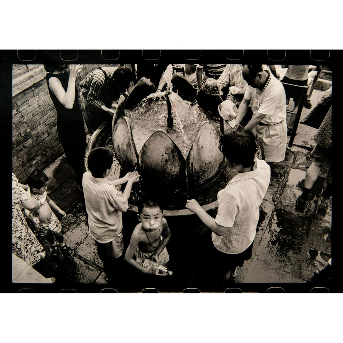 David Liu (American, b. Hong Kong 1958) Signed: Selenium toned silverprint; depicting group of people drinking from a public water fountain. Artist signed in pencil on verso. Unframed. Good condition. Dimensions: 16"H x 20"W (40.6cm x 50.8cm). (t.3