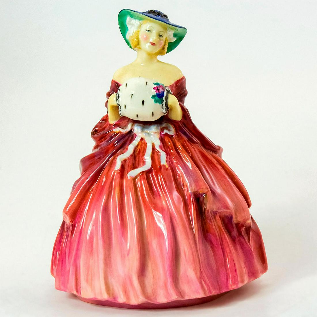 Genevieve HN1962 - Royal Doulton Figurine: Bone China. Genevieve wears a voluminous red dress, a blue and green hat, and a fur muff. Series: Harradine Classics. Royal Doulton backstamp. Artist: Leslie Harradine Issued: 1941 - 1975 Dimensions: 
