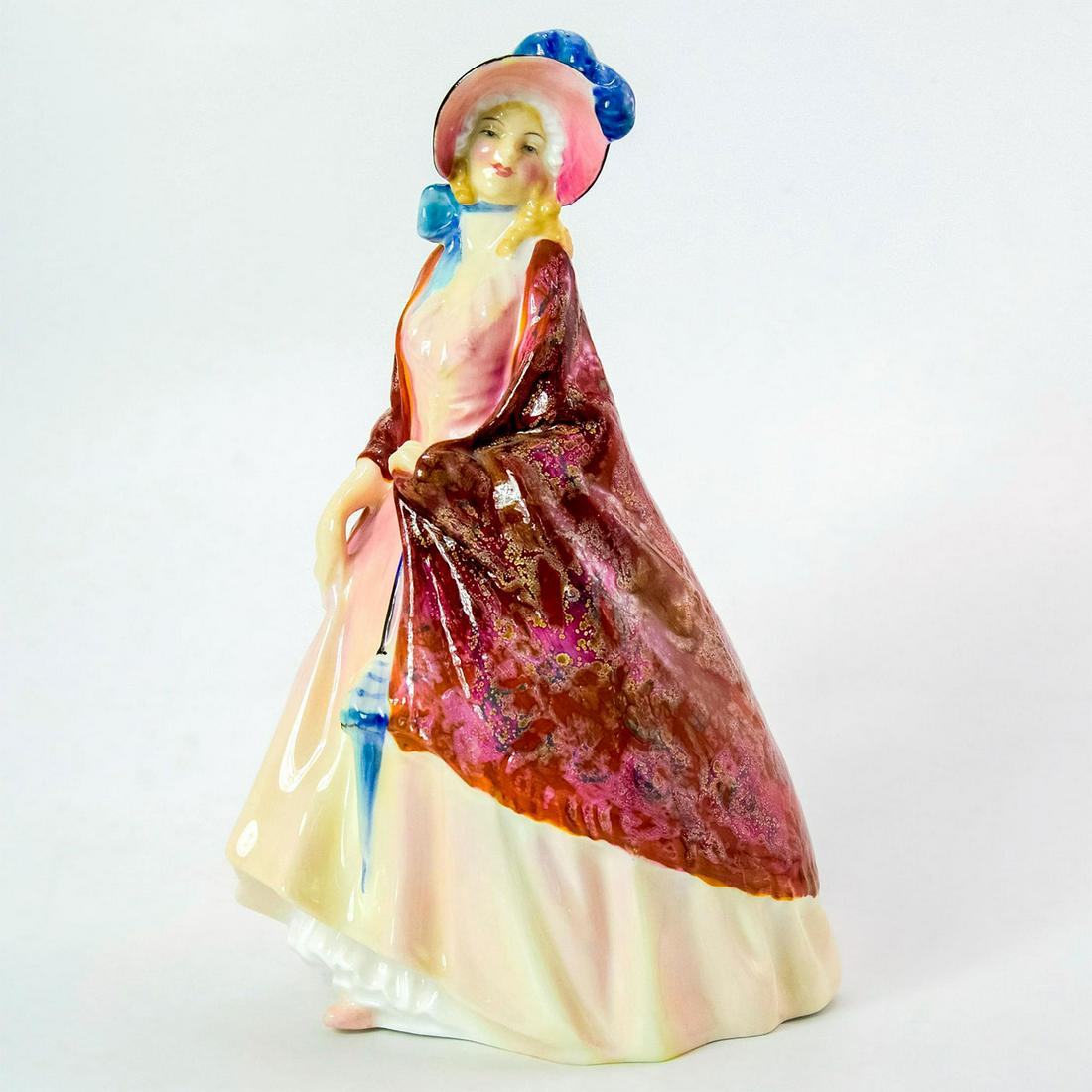 Paisley Shawl HN1987 - Royal Doulton Figurine: Bone China. She wears a cream dress and red patterned shawl, complete with a black bonnet tied with a blue bow. Series: Harradine Classics. Royal Doulton backstamp. Artist: Leslie Harradine Issued: 19