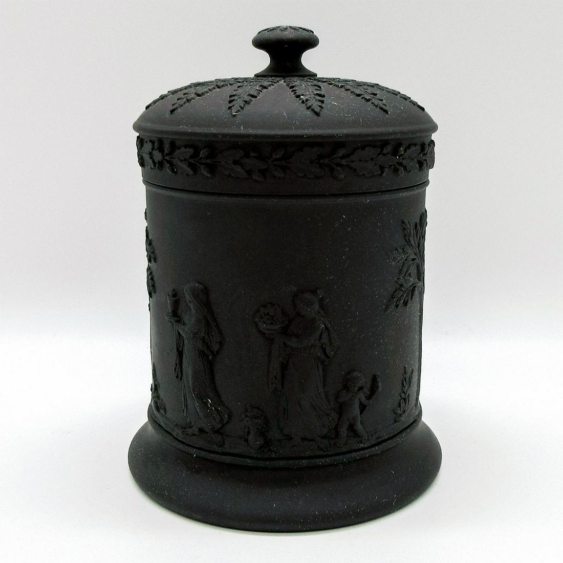 Wedgwood Black Jasperware Cigarette Jar: Lidded cigarette jar with relief Neoclassical design encircling body; foliate borders. Wedgwood impressed backstamp. Rim restored. #cigarettejar Issued: 20th c. Dimensions: 4.5"H Manufacturer: Wedgwoo