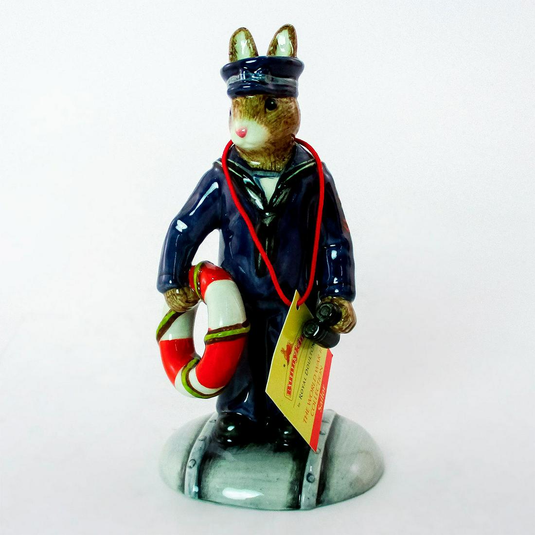 Sailor DB370 - Royal Doulton Bunnykins: Bunny in dark blue and white naval uniform with red and white life saver on grey base. With certificate. The World War II Collections. Royal Doulton backstamp. Original box. Weight: 3.5oz Issued: 2005