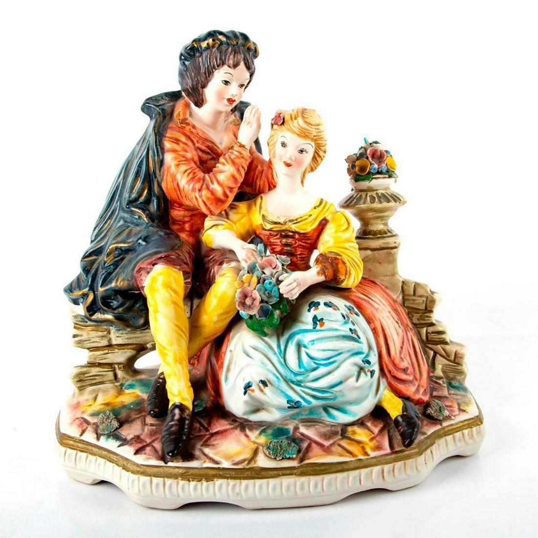 Vintage Italian Style Figurine Grouping: Matte finish; Bright colors and stone style street. Man whispering to a woman. Marked as Capodimonte, repaired hand and arm. Issued: 20th c. Dimensions: 12"L x 12"H Country of Origin: Italy