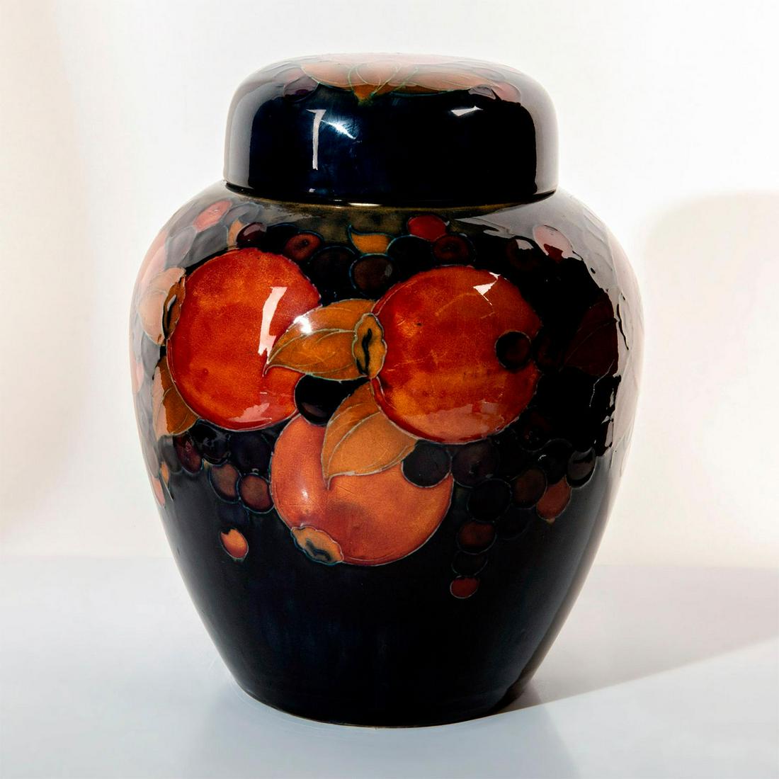 Moorcroft Pottery Large Lidded Ginger Jar, Pomegranate: Bulbous form, decorated with tube-lined designs of pomegranates and berries on a rich blue ground. Full William Moorcroft signature in blue to bottom base. Impressed Moorcroft to underside of cover. I