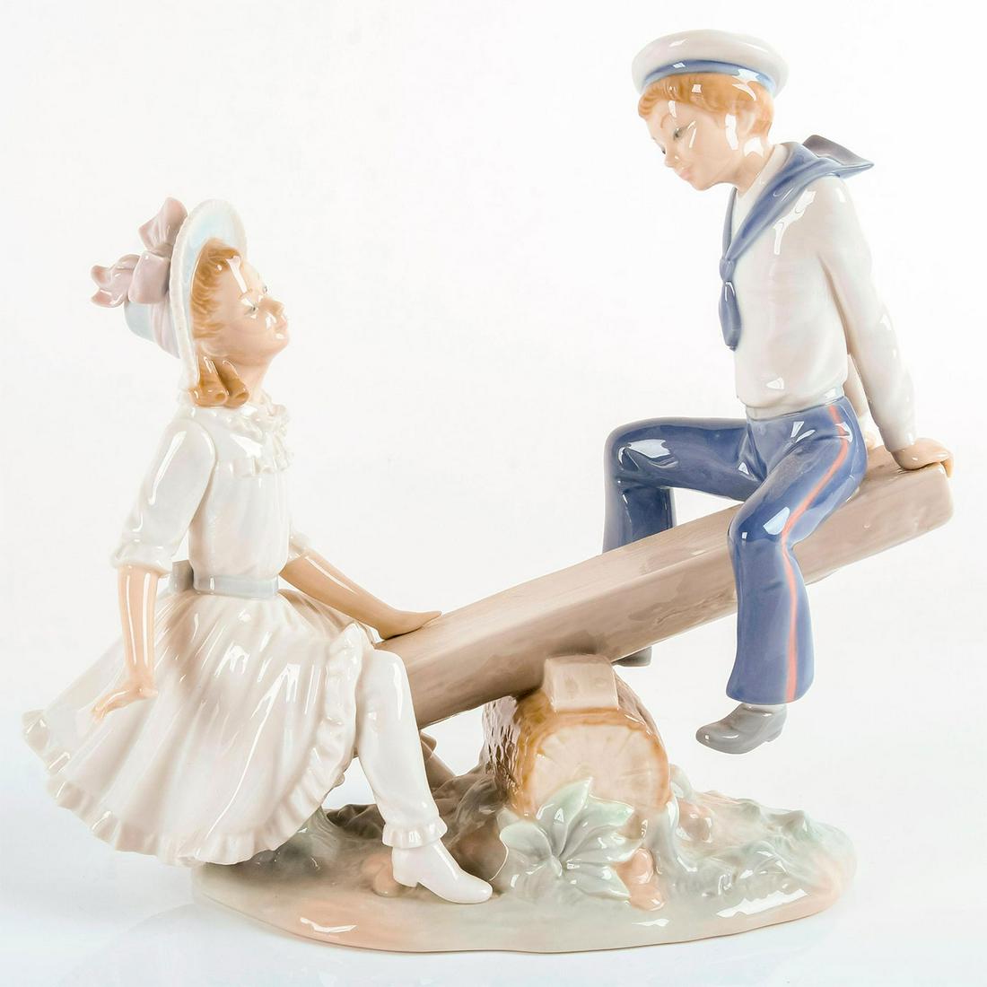 See-Saw 1001255 - Lladro Porcelain Figurine: Boy and girl on see-saw; Both wearing hats. Lladro backstamp on bottom. Artist: Vincente Martinez Issued: 1974-1991 Dimensions: 9.5"H Manufacturer: Lladro Country of Origin: Spain