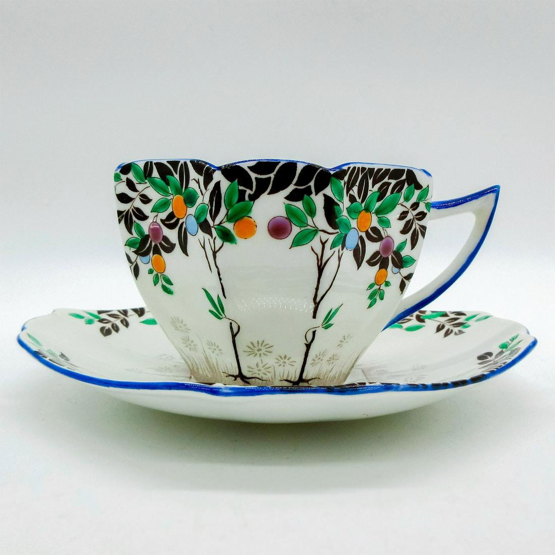 2pc Shelley Queen Anne Cup and Saucer, Black Trees 11697: Art Deco style bone china tea set; Black tree with orange, blue and purple fruits. Cobalt blue rim. Shelley England backstamp. 11697 hand-written on base. Cup size - 2.5"H x 3.5" diameter (widest). Sa