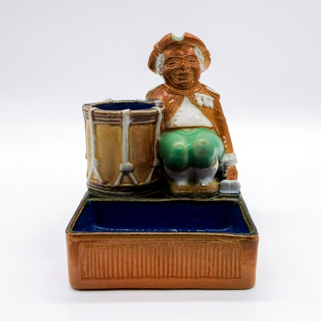Antique Doulton Lambeth Military Drummer Boy Match Stand: Brown, blue, green, and white stoneware match stand with a seated drummer beside a drum. Doulton Lambeth #DoultonLambeth #MatchStand #Dummer Issued: 1890s Dimensions: 4"L x 3.75"W x 4.75"H Manufacture