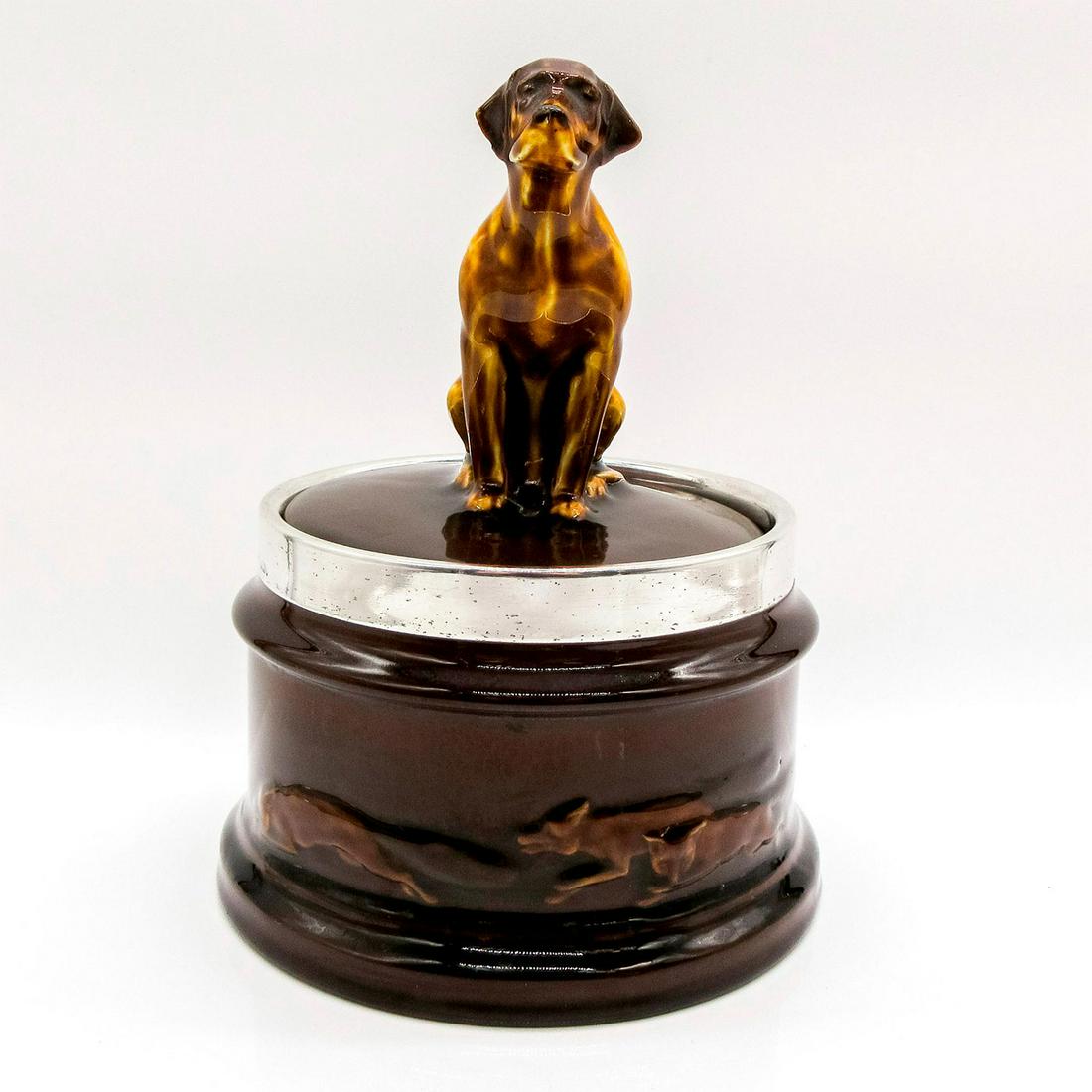 Lidded Tobacco Jar, Seated Foxhound - Royal Doulton Kingsware: Rare round shape jar; sterling silver rim. Foxhound finial, HN166 on lid. Relief of running foxes along the base.