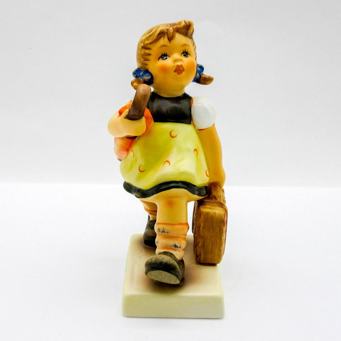 Goebel Hummel Figurine, Merry Wanderess: Porcelain hand painted figure of a young girl walking, holding a suitcase and umbrella. M J Hummel stamped to base; Goebel backstamp. In original box, 3.5"H x 5.75"W x 3.5"L. Issued: 21st c. Dimension