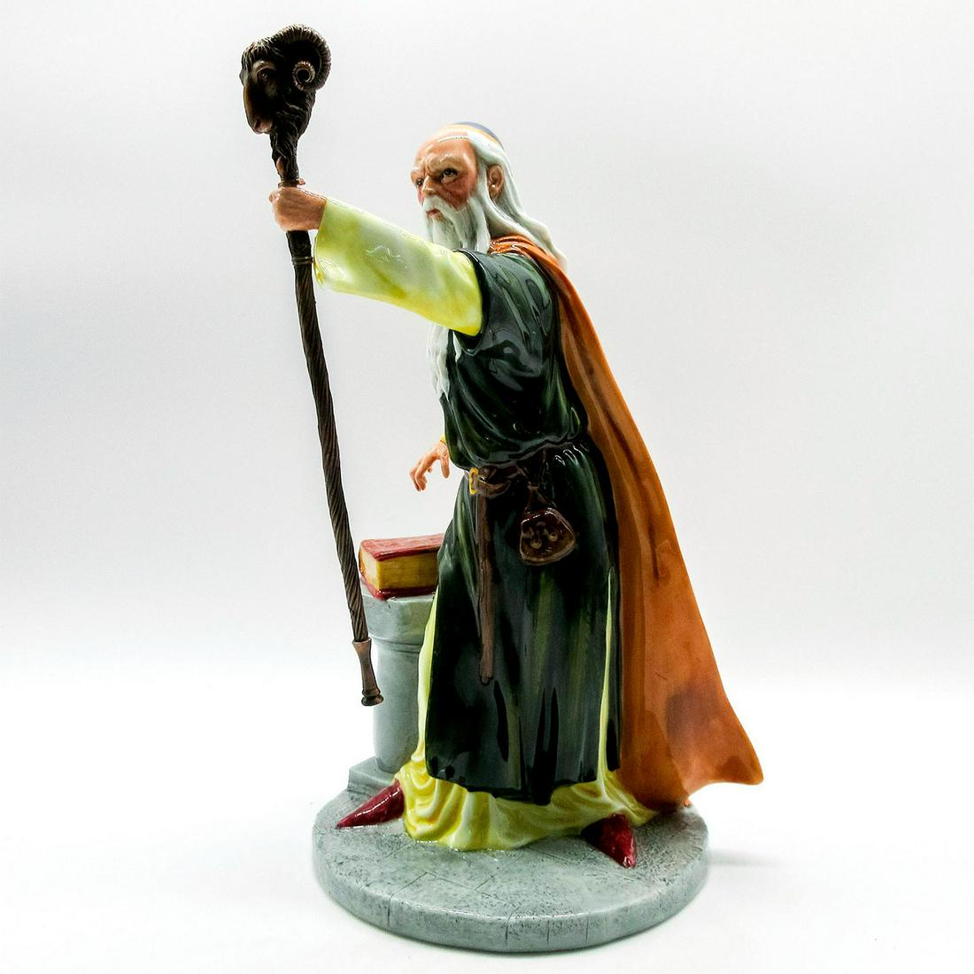 Merlin HN4540 - Royal Doulton Figurine: Merlin posing in green, orange and yellow attire. Holding staff in hand with book and pedestal by his side. Royal Doulton backstamp. Artist: Shane Ridge Issued: 2003 Dimensions: 9.75"H Edition Number: