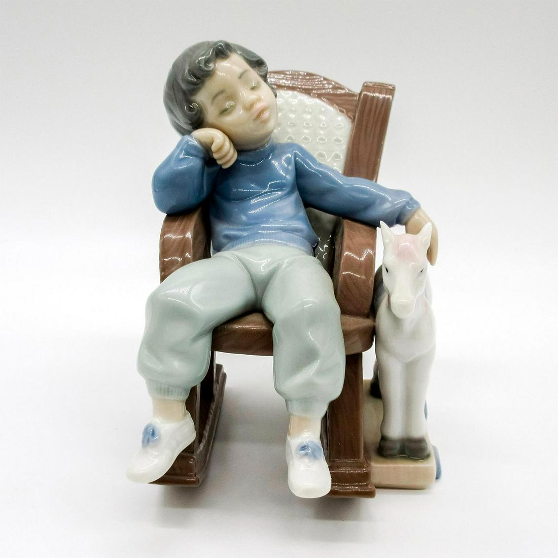 All Tuckered Out 1005846 - Lladro Porcelain Figurine: Glossy finish; Lladro backstamp. A child snoozing in a rocking chair with a rocking horse. Includes original box: 7.25"L x 4.5"W x 7.75"H. Artist: Jose Puche Issued: 1992-2004 Dimensions: 4.75"H Manuf