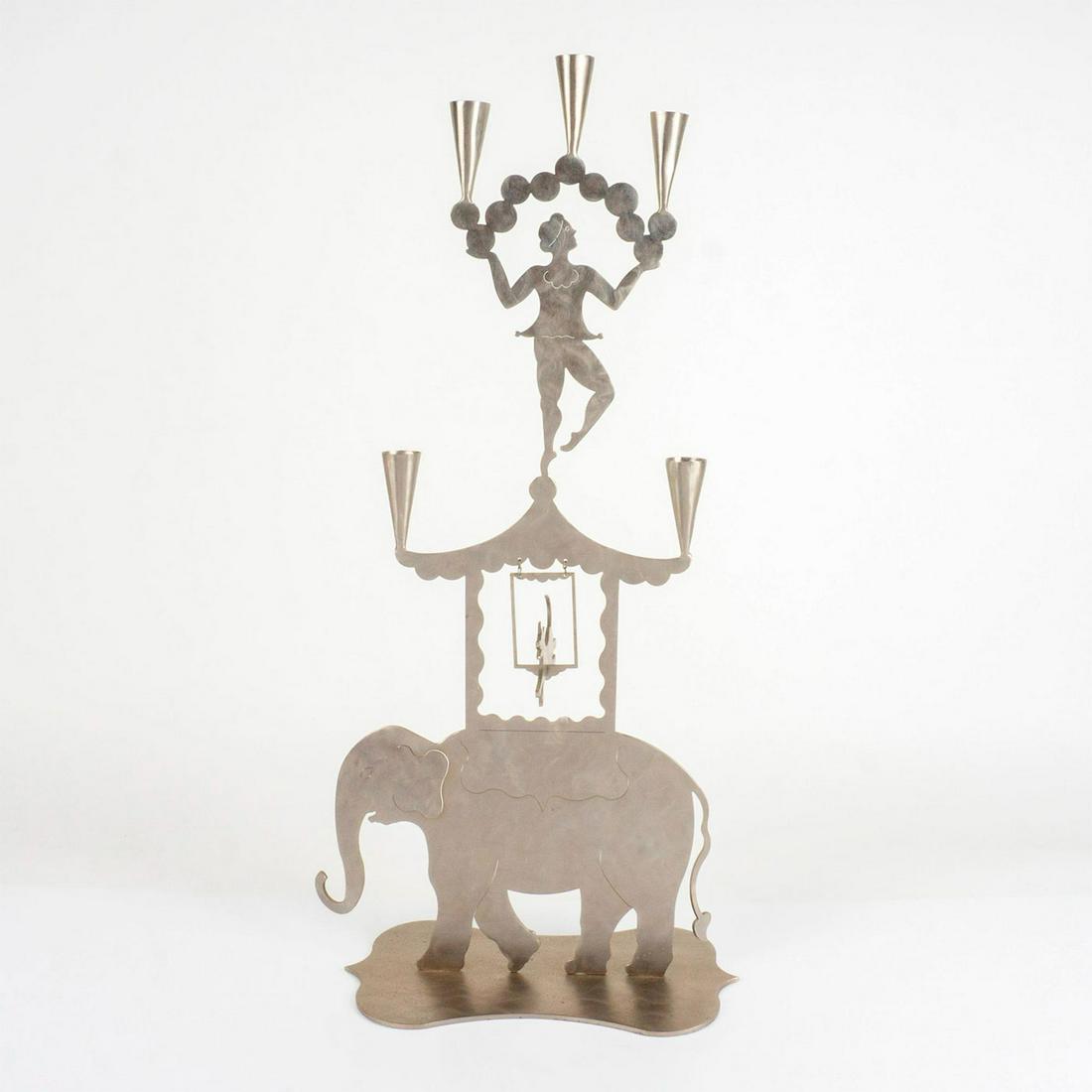 Amy Hess-Ark NY Metal Circus Candle Stand: A charming 5 capital candle stand depicting a dog jumping over an elephant and a performer juggling. Amy Hess-Ark NY 95 engraved on the base. Artist: Amy Hess-Ark Issued: 1995 Dimensions: 13.5" L x 6.