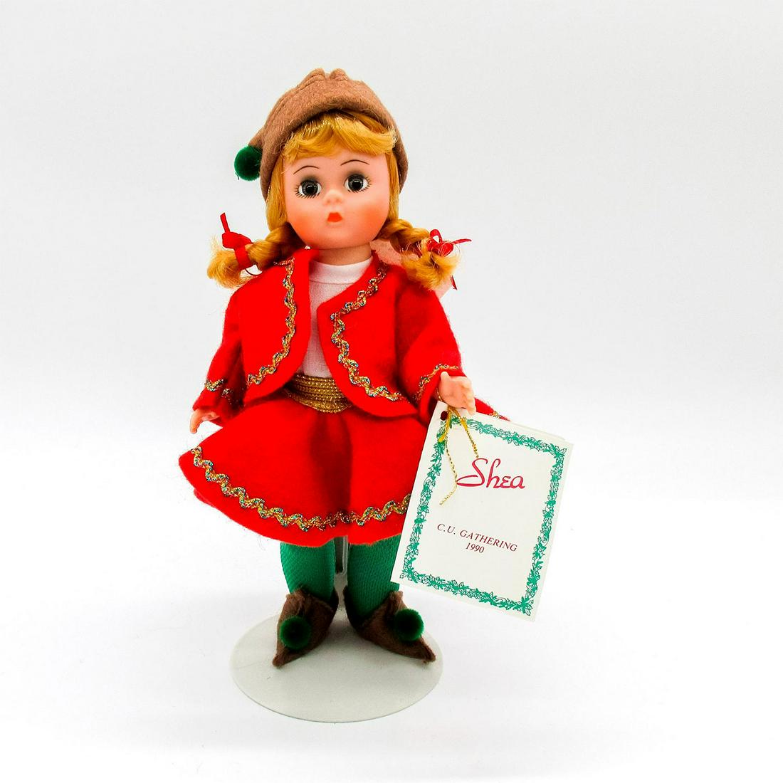 Vintage Madame Alexander Doll, Shea: Vintage doll with braided blonde hair. Red and green felt Christmas outfit with pointed elf shoes. Stand included. Madame Alexander tags. Issued: 1990 Dimensions: 8" H Manufacturer: Madame Alexander C