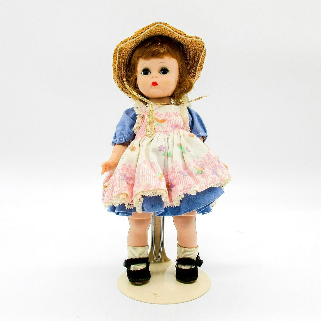 Vintage Madame Alexander Doll, Alexander-kin: Vintage doll with short curly hair. Periwinkle blue dress with butterfly patterned pinafore. Straw sunhat included. Part of the Alexander-kins collection. Stand included. Madame Alexander tags. Issued