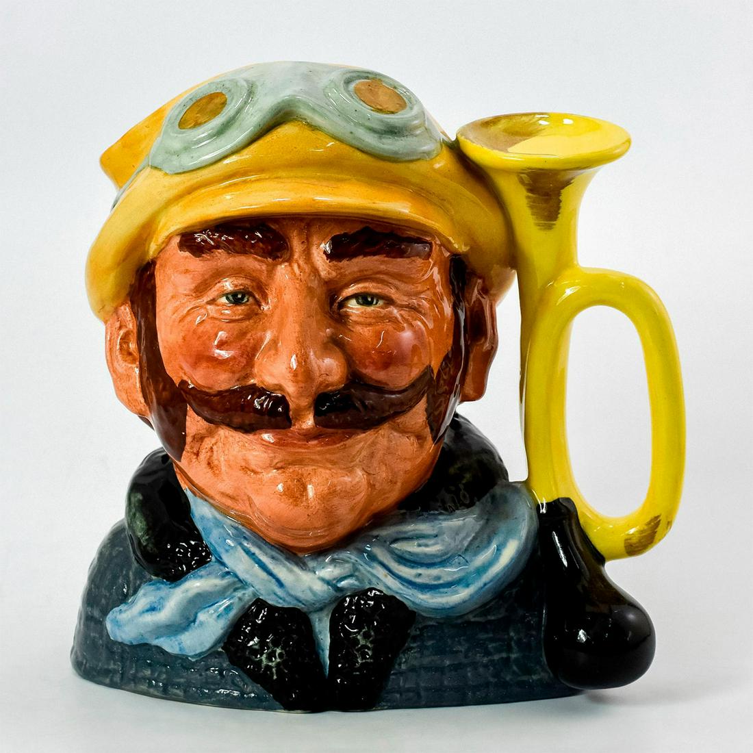 Veteran Motorist D6633 - Large - Royal Doulton Character Jug: Yellow hat, green coat, white scarf. Artist: David B. Biggs Issued: 1973 - 1983 Dimensions: 7.5"H Manufacturer: Royal Doulton Country of Origin: England