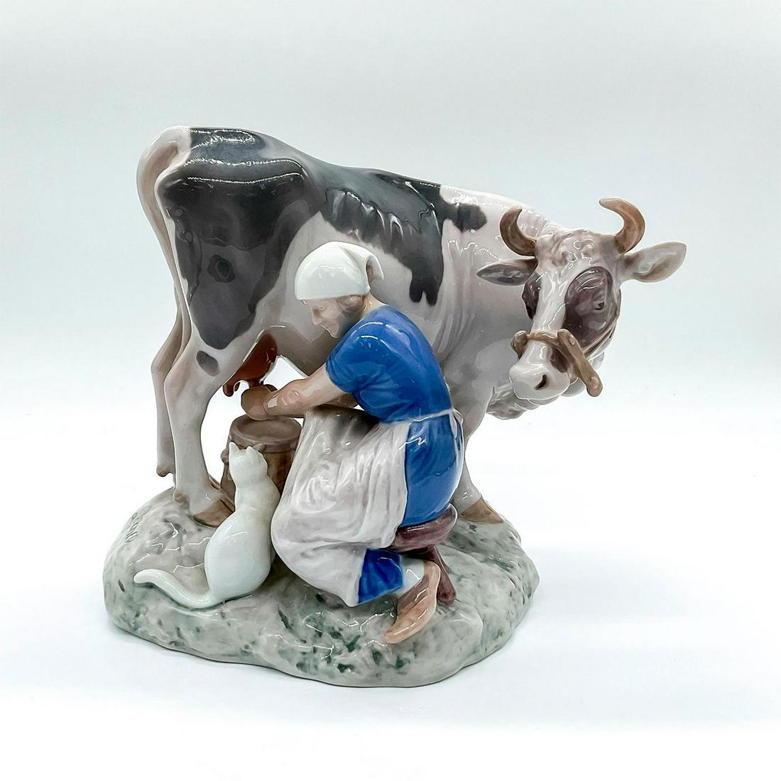 Bing and Grondahl Porcelain Figurine, The Milk Maid: Group figure of a famer milking a cow and smiling at a white cat at her feet. 2017; Bing and Grondahl backstamp. Artist's signature on the side. Artist: Axel Locher Issued: c. 1948-1951 Dimensions: 8.