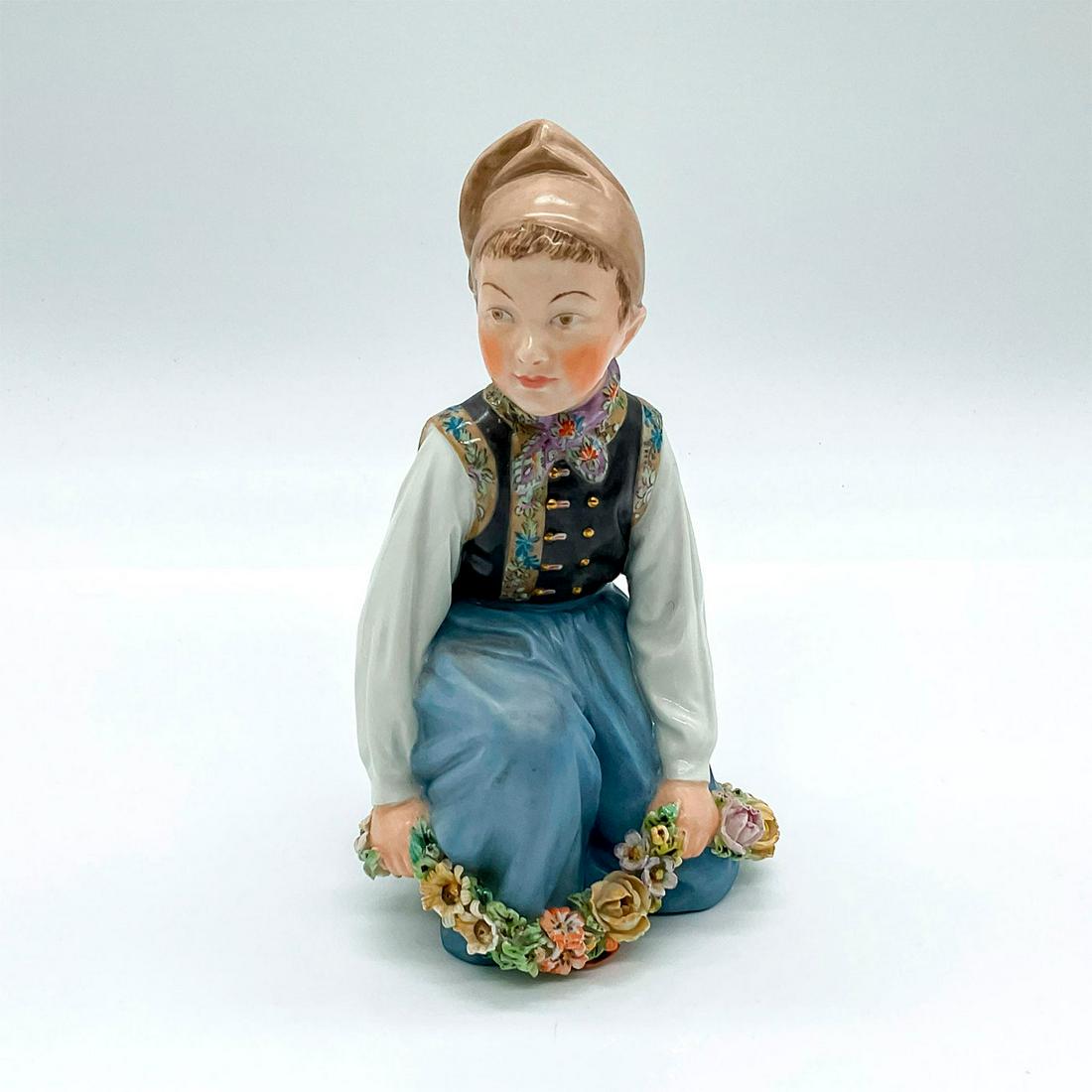 Royal Copenhagen Porcelain Figurine, Amager Boy: Figure of a young Danish boy holding a garland of flowers. 12414; Royal Copenhagen backstamp. Artist: Carl Martin-Hansen Issued: c. 1953 Dimensions: 3.5"L x 3.25"W x 5.75"H Manufacturer: Royal Copenha