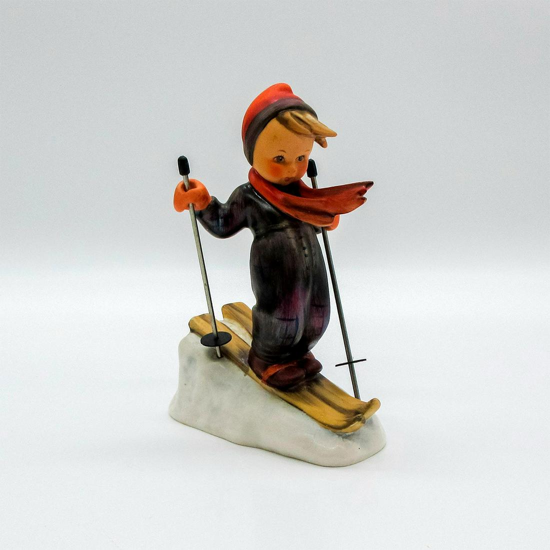 Goebel Hummel Figurine, Skier: Boy in red and black winter outfit riding skis. Metal ski poles included. Germany on bottom of piece. M. I. Hummel inscribed on base. Goebel backstamp. Artist: Reinhold Unger Issued: 1950 Dimensions: