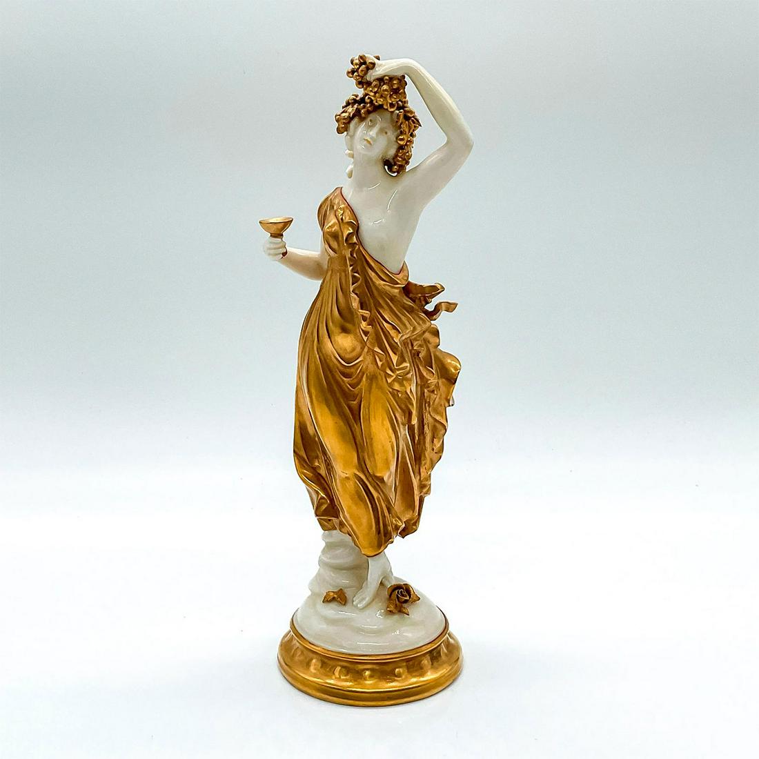 Capodimonte Style Golden Maiden Figure: Maiden dressed in a golden toga and garland of grapes in her hair. Standing on a base with a swirl design. Blue crown over N backstamps. Dimensions: 2.75"L x 3"W x 8.5"H