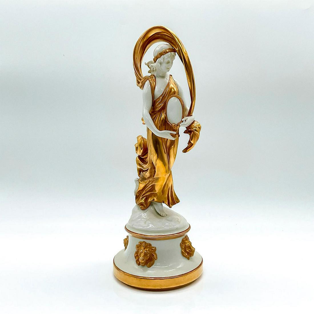 Capodimonte Style Golden Maiden Statuette: A maiden in a gilded dress, holding a mirror. Standing on a round base with golden lion head reliefs. 7 prong blue crown over N backstamp. Dimensions: 4"L x 4.5"W x 10.5"H
