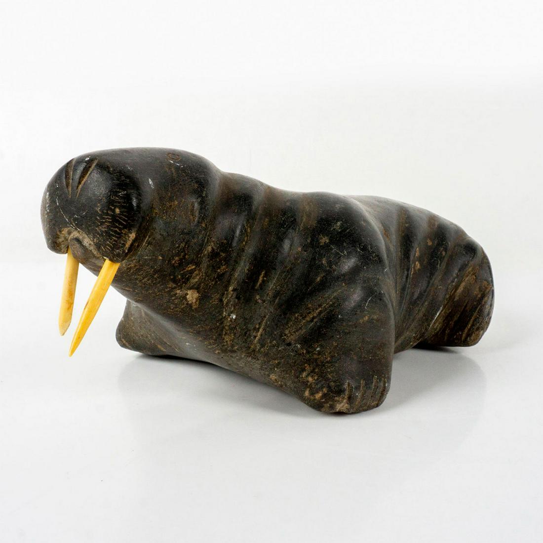 Hand-Carved Inuit Soapstone Sculpture, Walrus: Black soapstone walrus sculpture with muscular body, incised facial details, and bone tusks. Unsigned. Dimensions: 8.75"L x 4.5"W x 3.25"H