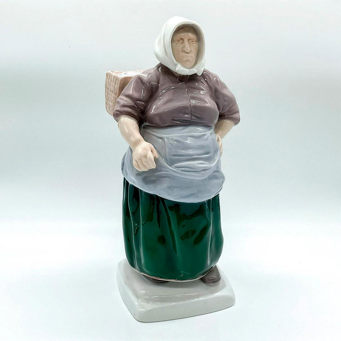 Bing and Grondahl Porcelain Figurine, Fishwife: Figure of a woman carrying a basket of fish. Dressed in a lavender shirt and green skirt with a blue apron. 1702; Bing and Grondahl backstamp. Artist: Kai Nielsen Issued: c. 1948-1951 Dimensions: 5.5"
