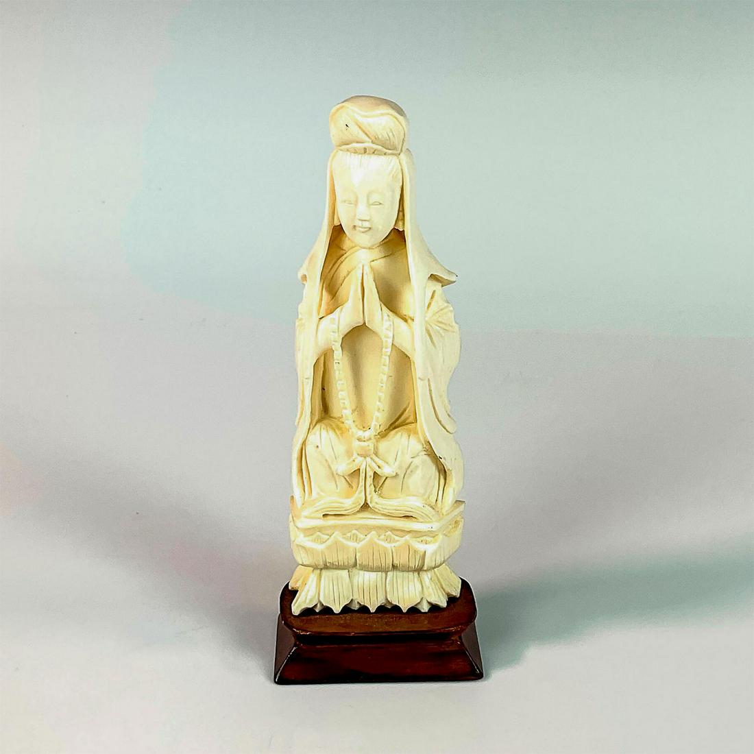 Chinese Carved Bone Guanyin Sculpture with Base: A beautiful figure of the Bodhisattva seated on a lotus blossom with her palms pressed together. Attached on a wooden base. Dimensions: 2"L x 1.25"W x 5.5"H Country of Origin: China