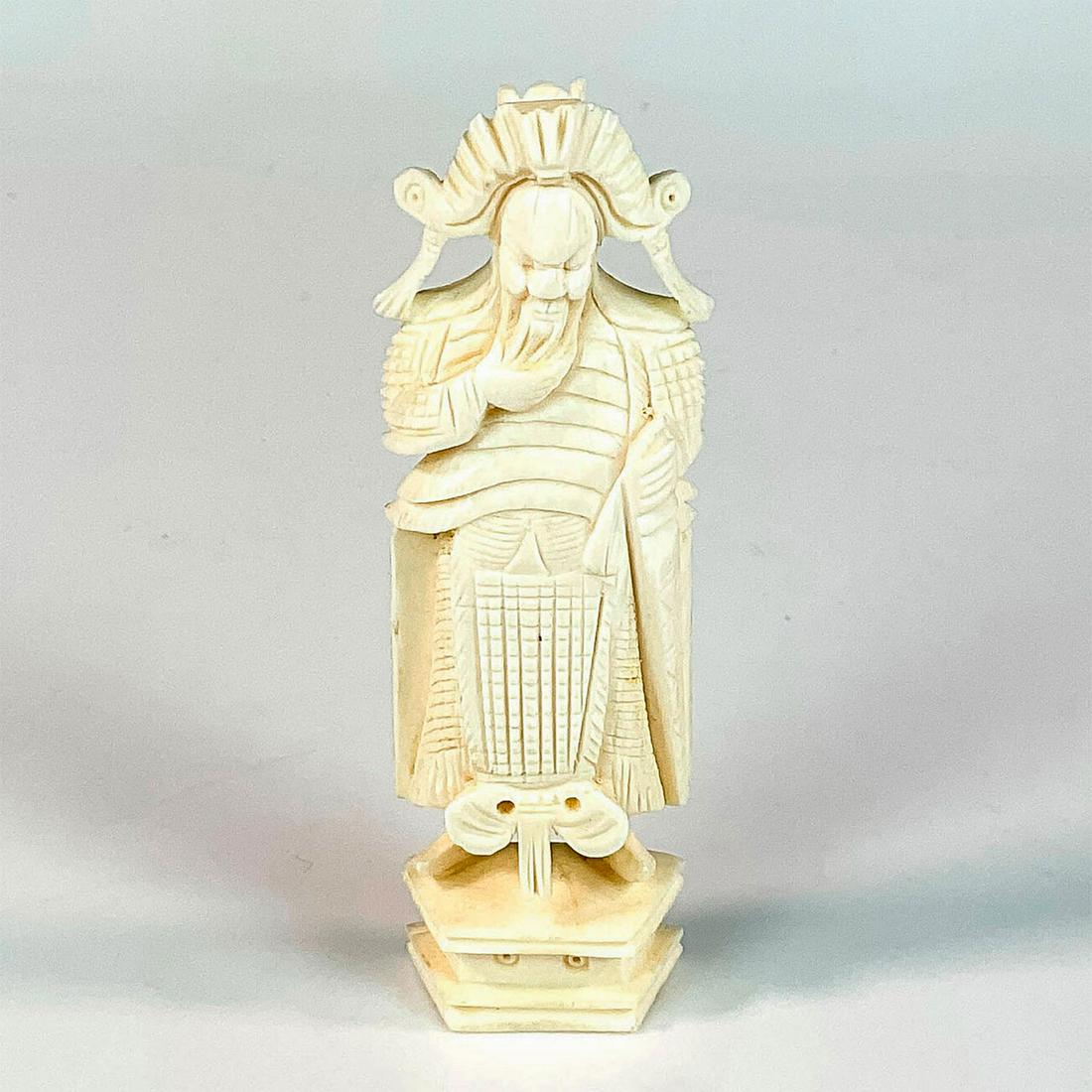 Chinese Small Carved Bone Guan Gong Figurine: A figure of the once mortal general turned deity after his death. The God of War stands on a pedestal in full armor and hand on his beard. Dimensions: 1.25"L x 0.75"W x 4"H Country of Origin: China