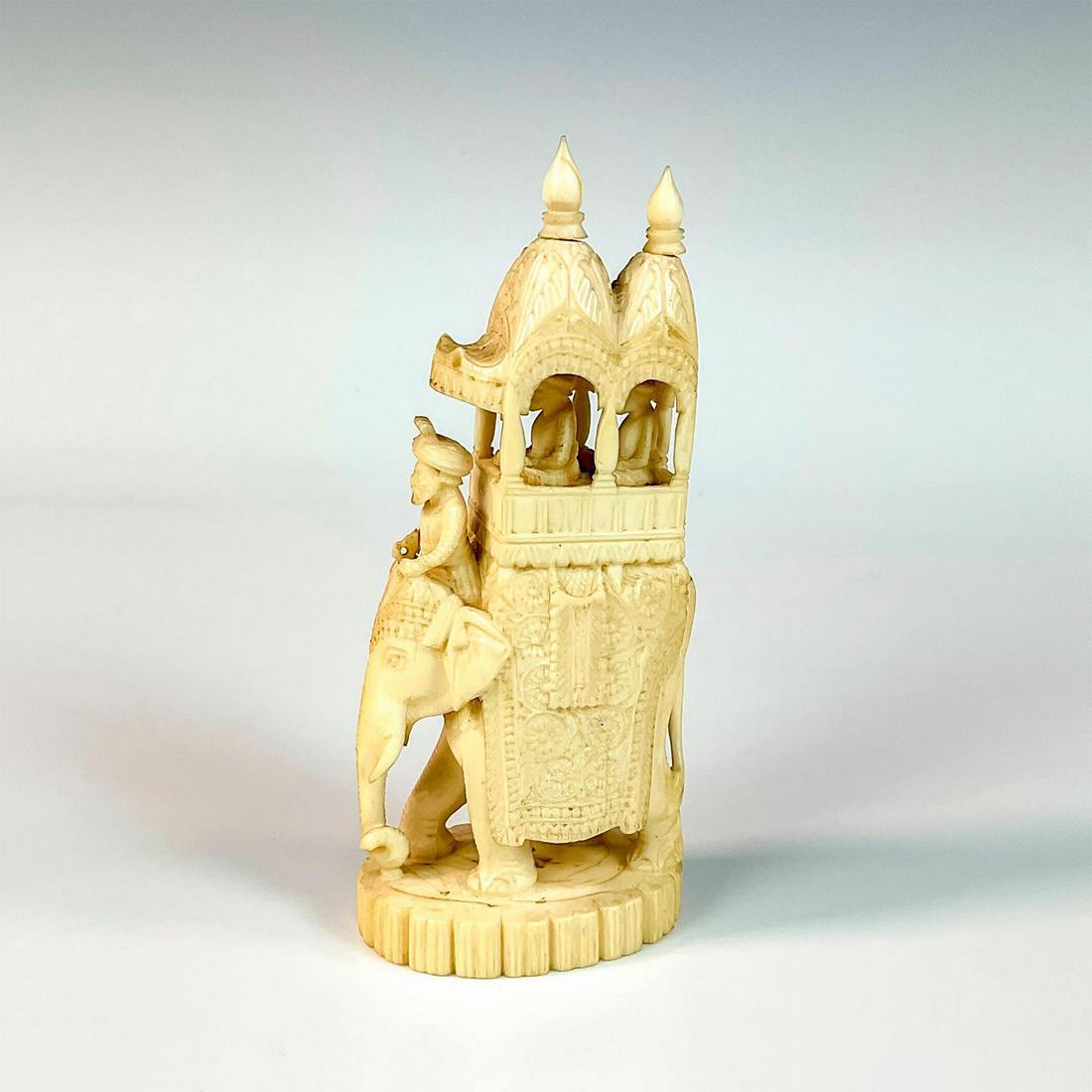 Carved Bone Decorated Indian Elephant Figurine: Inspired by an artifact found in the Government Museum Jodhpur in Indian. The elephant figure is adorn with a floral design, a howdah with two passengers, and a mahout on the front. Dimensions: 2.5"L 