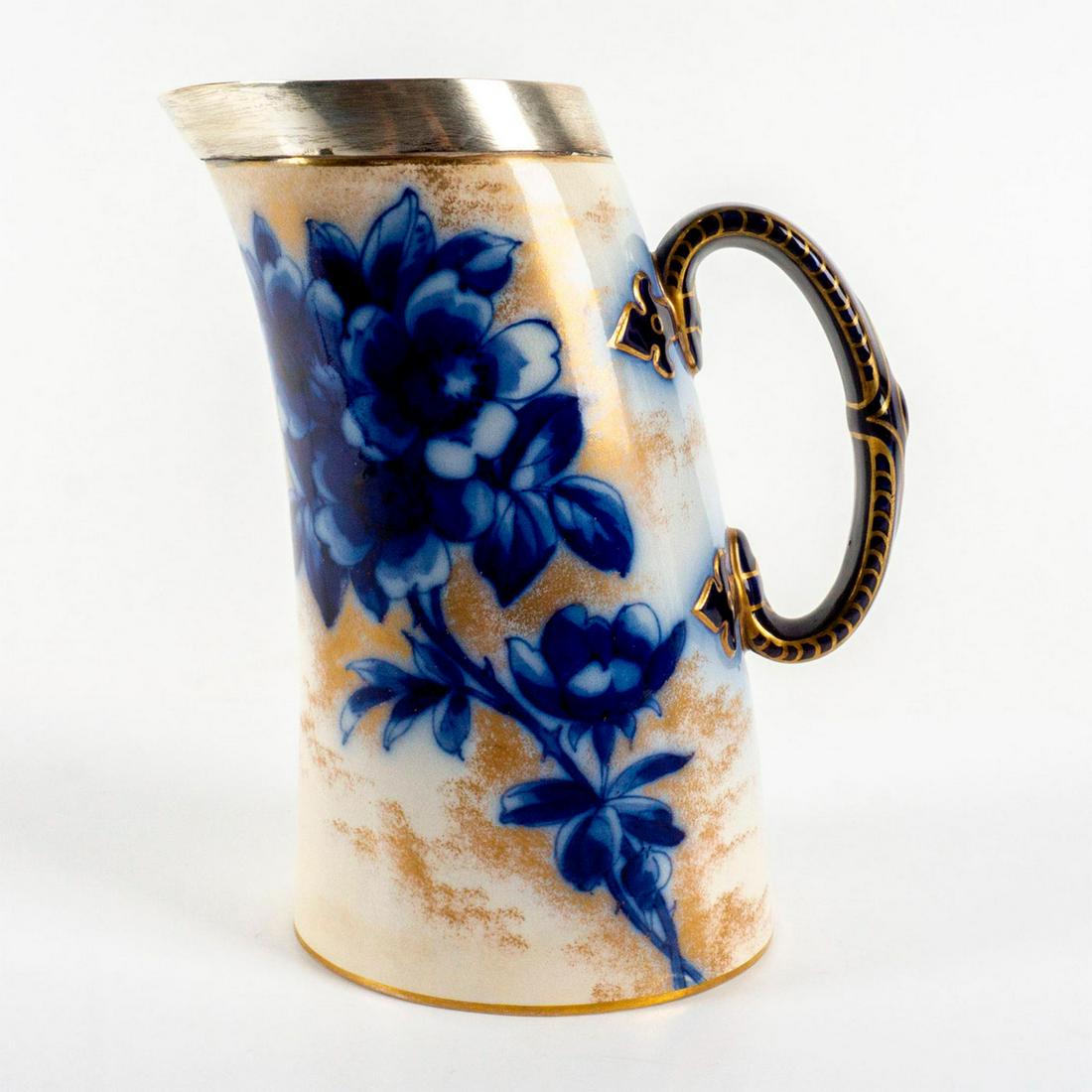Doulton Burslem Silver Hallmarked Blue Floral Motif Pitcher: Hand painted porcelain with cobalt blue flowers gold spray on a white background. Blue handle with gold painted pattern. Pitcher is rimmed with hallmarked sterling silver. Issued: 1886-1891 Dimensions